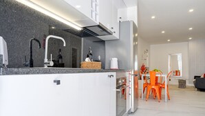 A modern kitchen with white cabinets, a granite countertop, and a built-in oven. There is a dining area with orange chairs and a table.