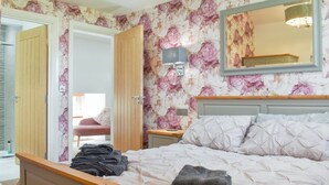 Una camera da letto con un letto, un comodino in legno, uno specchio e una porta che dà su un'altra stanza.