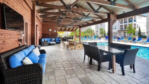 An outdoor covered patio with wicker furniture, a pool, and a view of the surrounding buildings. - August Dates Still Available! 5BR Luxury Home, Pool & Golf Cart • 3 Min to Beach (Miramar Beach)