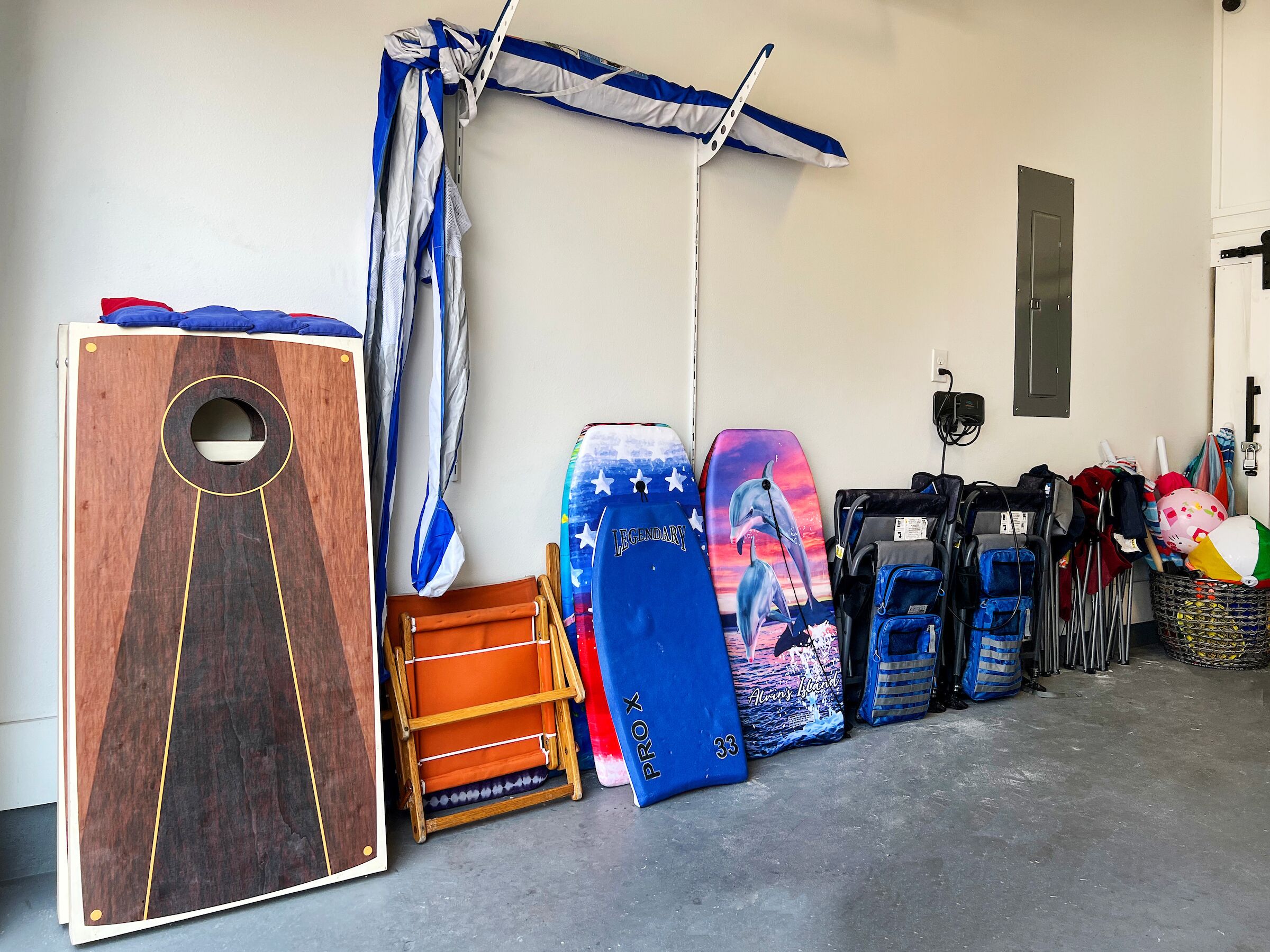 A storage area with various boards and equipment, including a wooden board with a circular cutout, a blue board with a dolphin design, and several blue and black bags.
