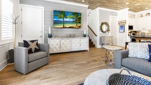A modern living room with a grey sofa, a white cabinet, and a painting of a beach scene. - August Dates Still Available! 5BR Luxury Home, Pool & Golf Cart • 3 Min to Beach (Miramar Beach)