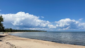 Ein Strand mit sandigem Ufer, ruhigem Wasser und bewaldeter Küstenlinie im Hintergrund.