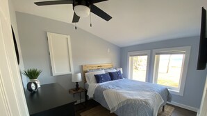 Ein Schlafzimmer mit Bett, Nachttischen, Deckenventilator, Fenster und Blick ins Freie.