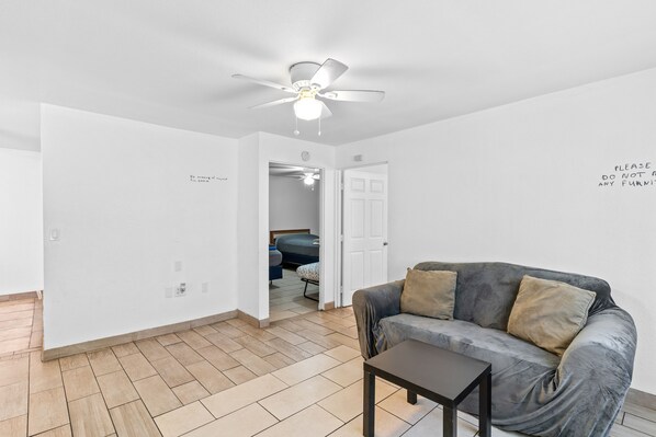 A living room with a grey sofa, a small table, and a ceiling fan.