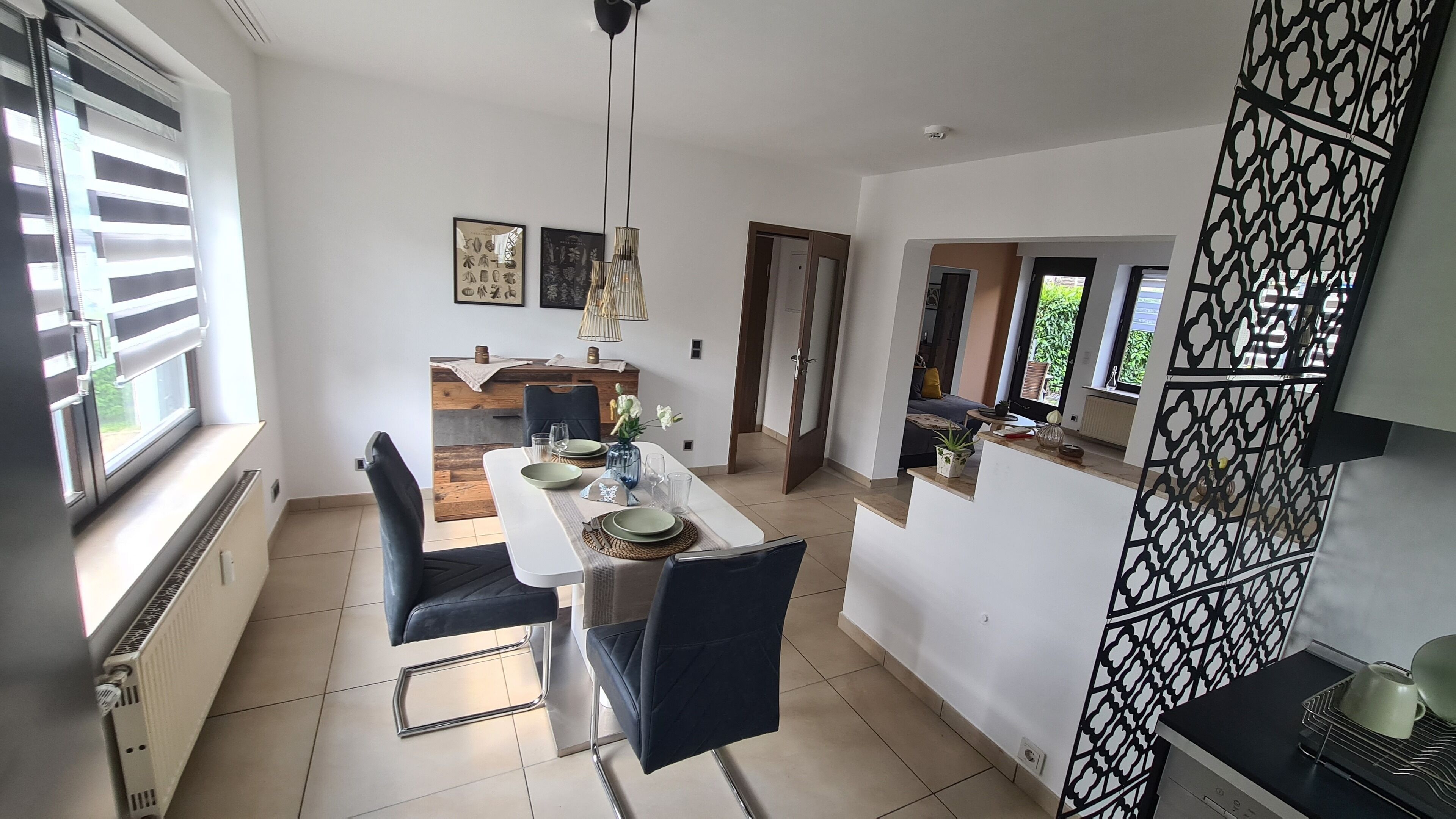 A modern dining area with a white table, black chairs, and a view of the adjacent living room.