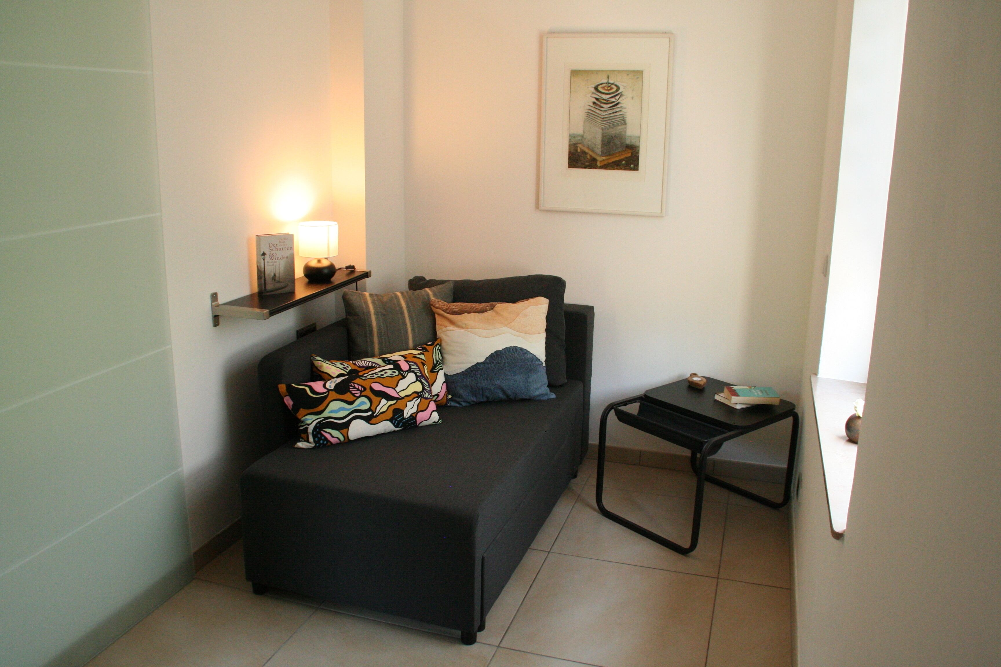 A small, modern living room with a sofa, a side table, and a framed picture on the wall.