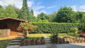 Una cabaña de madera con fachada de ladrillo, rodeada de un jardín cuidado con diversas plantas y flores.