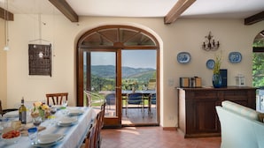 A dining area with a table set for four, a wooden cabinet, and a view of the outdoors. - Villa Olivi Pool by Geco Vacation Rentals (Pergine Valdarno)