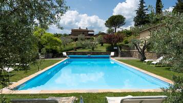 Relax by the serene pool surrounded by lush greenery and mature trees, perfect for sunbathing or reading.