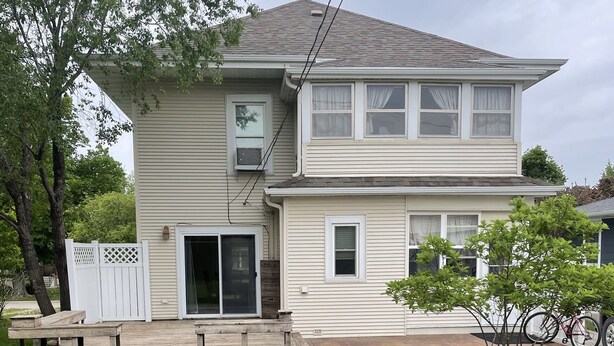A two-story house with a front porch, a garage door, and a small front yard with a lawn and some shrubs. - House close to Pine Lake and bike trails. (Eldora)