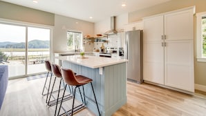 A modern kitchen with a large island, bar stools, and a view of the outdoors. - Charming Florence Home w/ Fire Pit & River Views! (Florence)