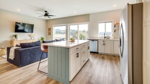 A modern kitchen with a central island, white cabinetry, and a built-in dishwasher. - Charming Florence Home w/ Fire Pit & River Views! (Florence)