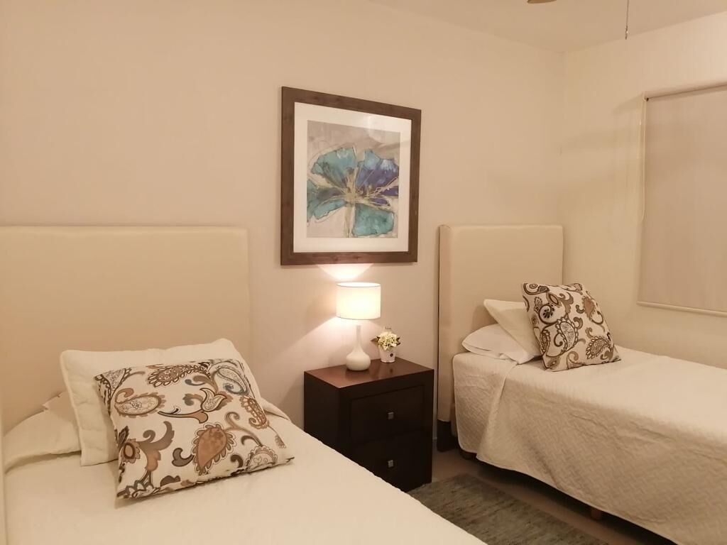 A hotel room with two beds, a nightstand with a lamp, and a framed artwork on the wall.