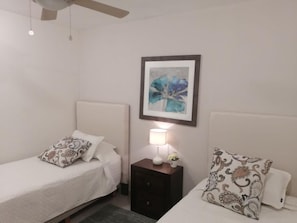 Ein Schlafzimmer mit zwei Einzelbetten, einem Nachttisch mit Lampe und einem gerahmten Kunstwerk an der Wand.