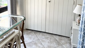 Una habitación con una puerta blanca, una mesa de vidrio, sillas de mimbre, una lámpara y un cartel en la pared que dice 'beach'.