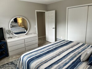 Un dormitorio con una cama, un aparador con espejo, un televisor y una puerta que da a otra habitación.