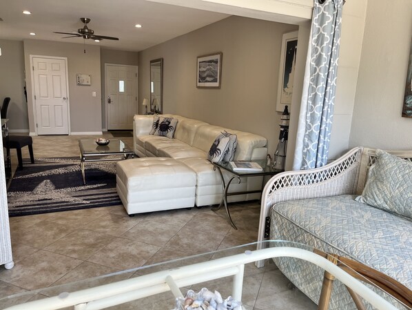 A spacious living room with a white leather sofa, a glass coffee table, and a wicker chair.