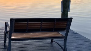 Un banco de madera en un muelle con un cuerpo de agua tranquilo al fondo y un atardecer.