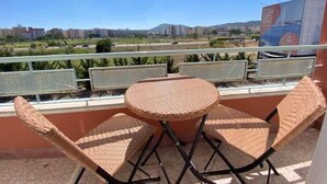 Un balcone con mobili in vimini, vista sulla città e un cartellone pubblicitario sullo sfondo.