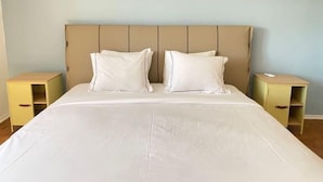 Un letto matrimoniale con testiera beige, due cuscini bianchi e due comodini con cassetti.