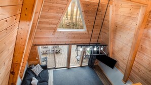 A wooden cabin with a loft bedroom, a balcony with a view of the forest, and a dining area. - Nature`s Nest Lakeside (Au Gres)