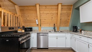 Een keuken met houten balken, een fornuis, magnetron, vaatwasser en witte kasten.