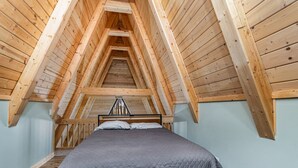 A bedroom with a sloped wooden ceiling, a bed with a gray quilt, and a metal headboard. - Nature`s Nest Lakeside (Au Gres)