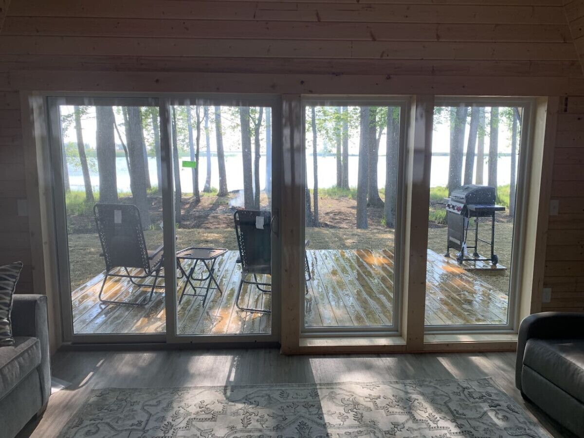 Una habitación con un amplio ventanal corredero que da a una terraza exterior con sillas y una parrilla.