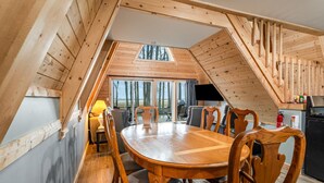 A wooden interior with a dining table, chairs, a TV, and a view of trees through a skylight. - Nature`s Nest Lakeside (Au Gres)