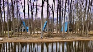 Une maison avec un toit bleu et un étang devant.