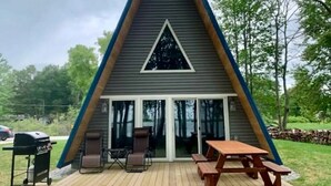 A triangular A-frame cabin with a patio area, outdoor seating, and a grill. - Stunning Sunrise Shore (Au Gres)