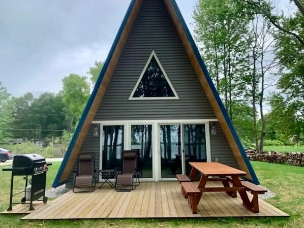 A triangular A-frame cabin with a patio area, outdoor seating, and a grill.