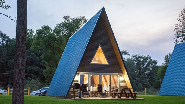 A modern, triangular-shaped building with a large glass entrance and outdoor seating area. - Stunning Sunrise Shore (Au Gres)