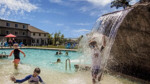 Una piscina con una cascada, rodeada por una valla y un edificio al fondo.