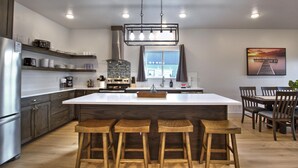 Una cocina moderna con una isla central, taburetes, sillas de madera y una mesa de comedor.