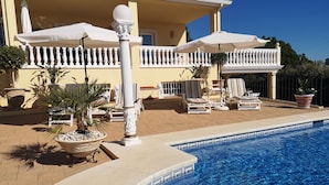 Un espace aménagé au bord de la piscine, avec des chaises longues, des parasols et des plantes en pot.