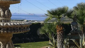 Un jardin agrémenté d’une fontaine en pierre, d’une statue de Bouddha et offrant une vue sur la mer et les montagnes.