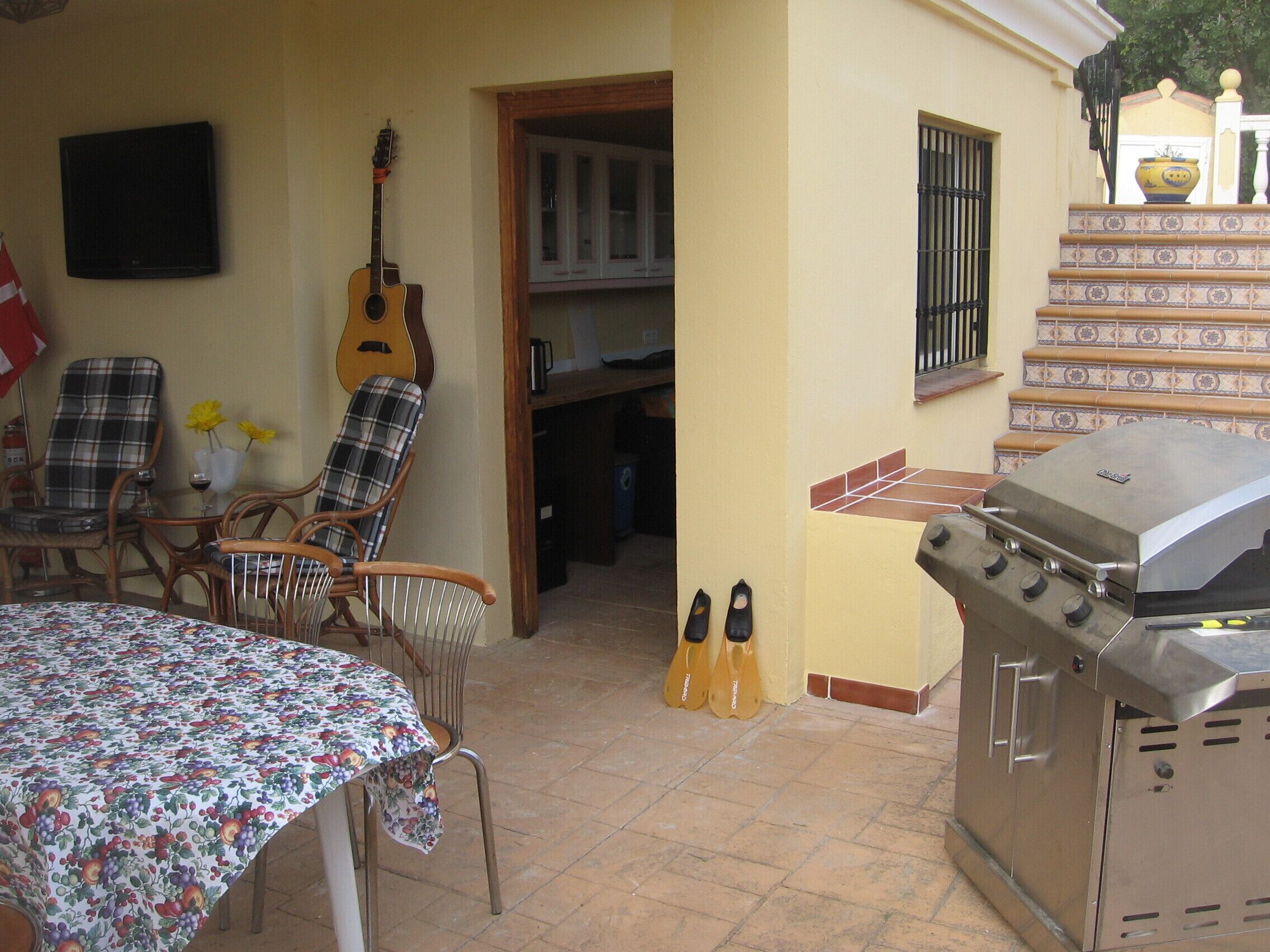 Une terrasse avec une table, des chaises, une guitare et un barbecue.