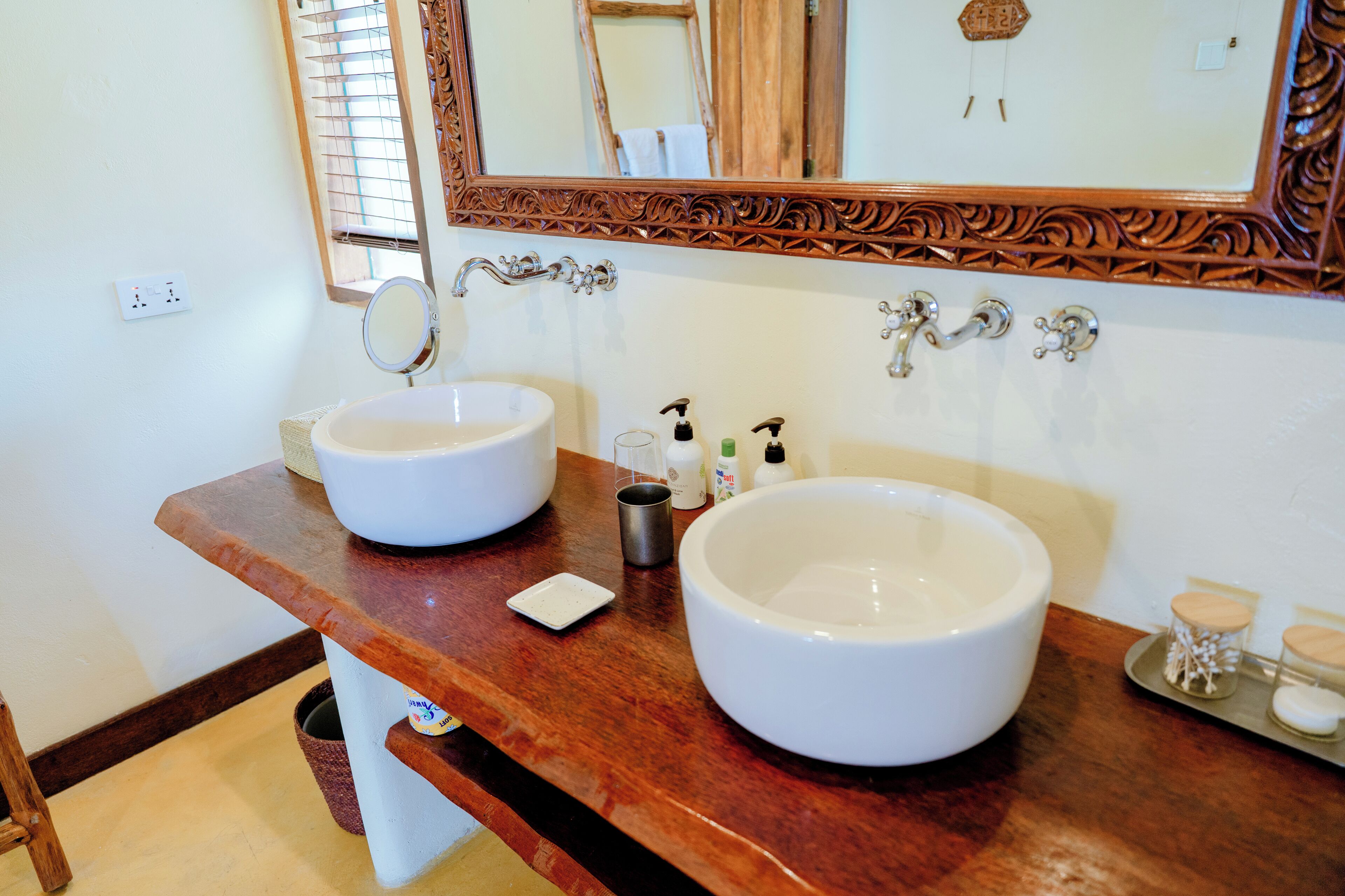 A bathroom with two large white sinks, a wooden vanity, a mirror, and a decorative mirror frame.