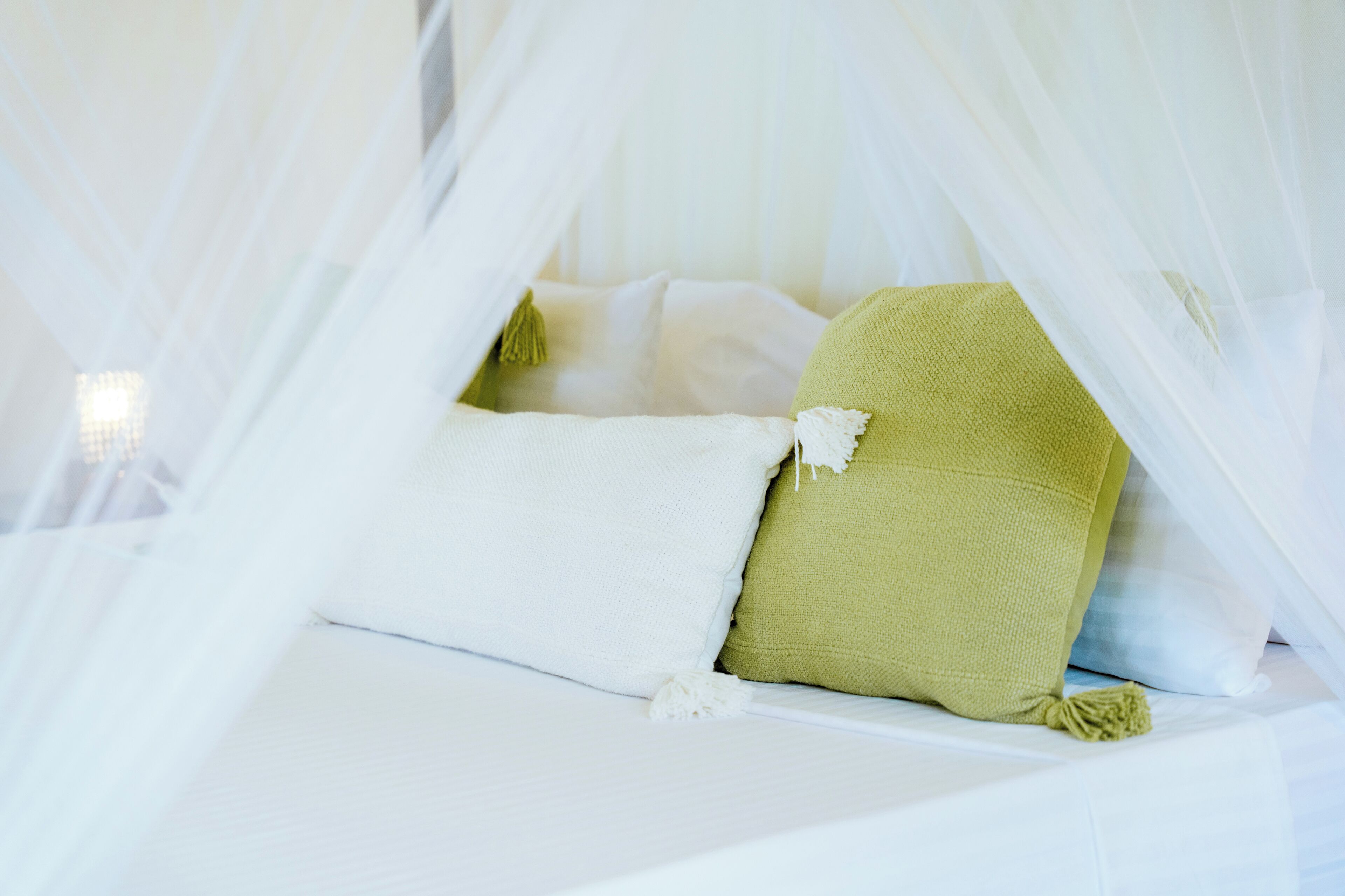 Una cama con ropa blanca y una almohada verde, parcialmente cubierta por un dosel blanco.
