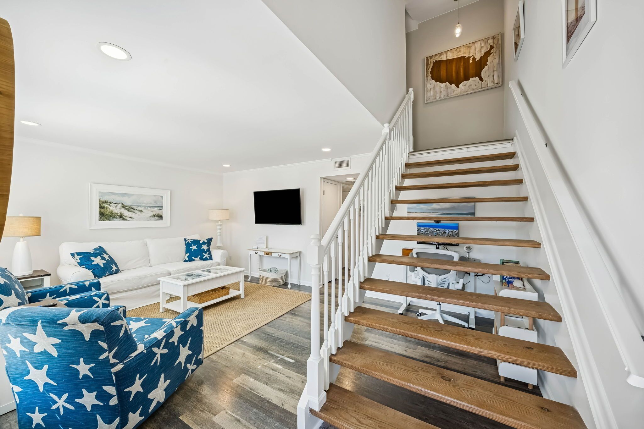 A modern living room with a white sofa, blue star-patterned armchair, wooden staircase, and a flat-screen TV mounted on the wall.