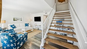 Una sala de estar moderna con un sofá blanco, un sillón azul estampado con estrellas, una escalera de madera y un televisor de pantalla plana montado en la pared.