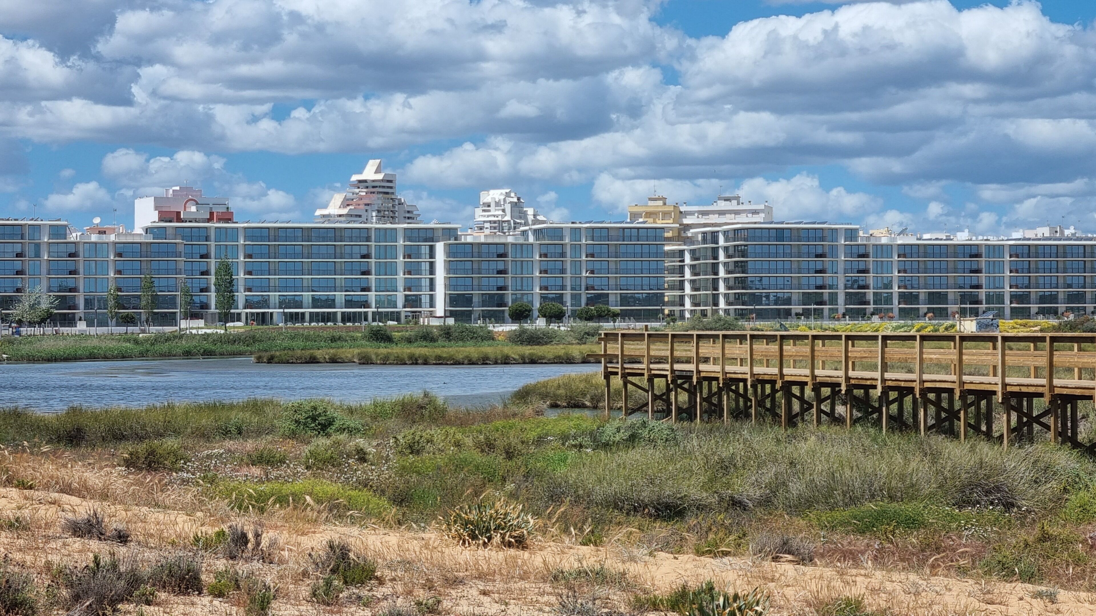 A modern hotel with multiple high-rise buildings, a waterfront view, and a wooden boardwalk.