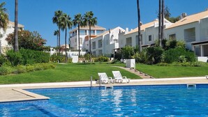 Ein Swimmingpool mit Liegestühlen, umgeben von Palmen und einem gepflegten Rasen.