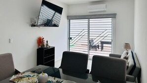 A modern living room with a glass door leading to a balcony, a flat-screen TV mounted on the wall, and a dining area with a table and chairs. - Napoles (Mazatlán)