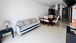 A modern living room with a sofa, dining table, chairs, a TV, and a lamp. - Napoles (Mazatlán)