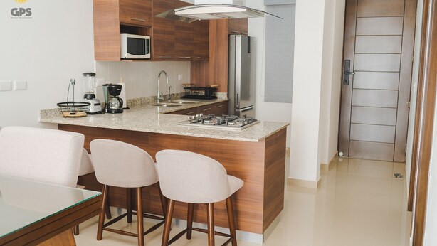 A modern kitchen with a central island, bar stools, a microwave, a refrigerator, and a coffee maker. - Napoles (Mazatlán)
