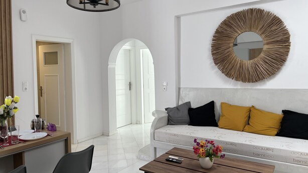 Een moderne woonkamer met een witte bank, een ronde spiegel en een eethoek met een tafel en stoelen.