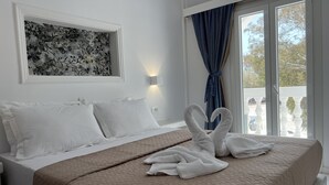 Hotelkamer met een bed, witte kussens, een beige geborduurde spreideken, een bloemig kunstwerk in een lijst aan de muur, een raam met uitzicht en een blauw gordijn.