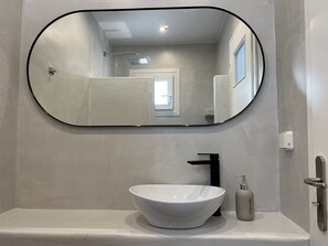 A bathroom with a white sink, a black faucet, a round mirror, and a dispenser. - 3 Bedroom House included car rental-Heated Jacuzzi (santorini)